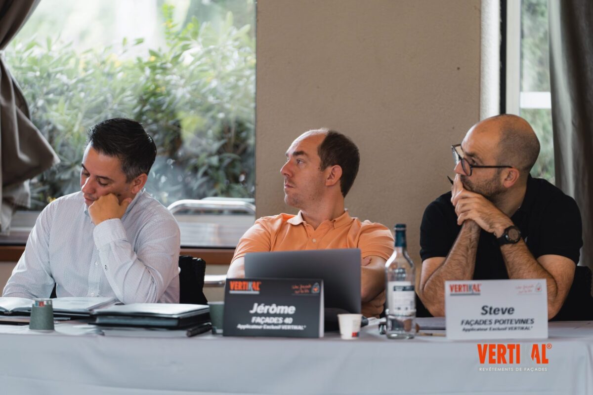 Trois hommes assis à une table de réunion avec des ordinateurs portables et des documents.