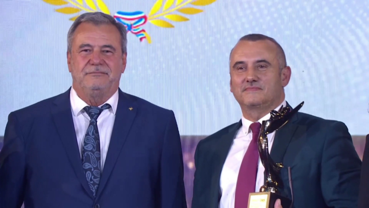 Deux hommes en costume, l'un tenant un trophée.