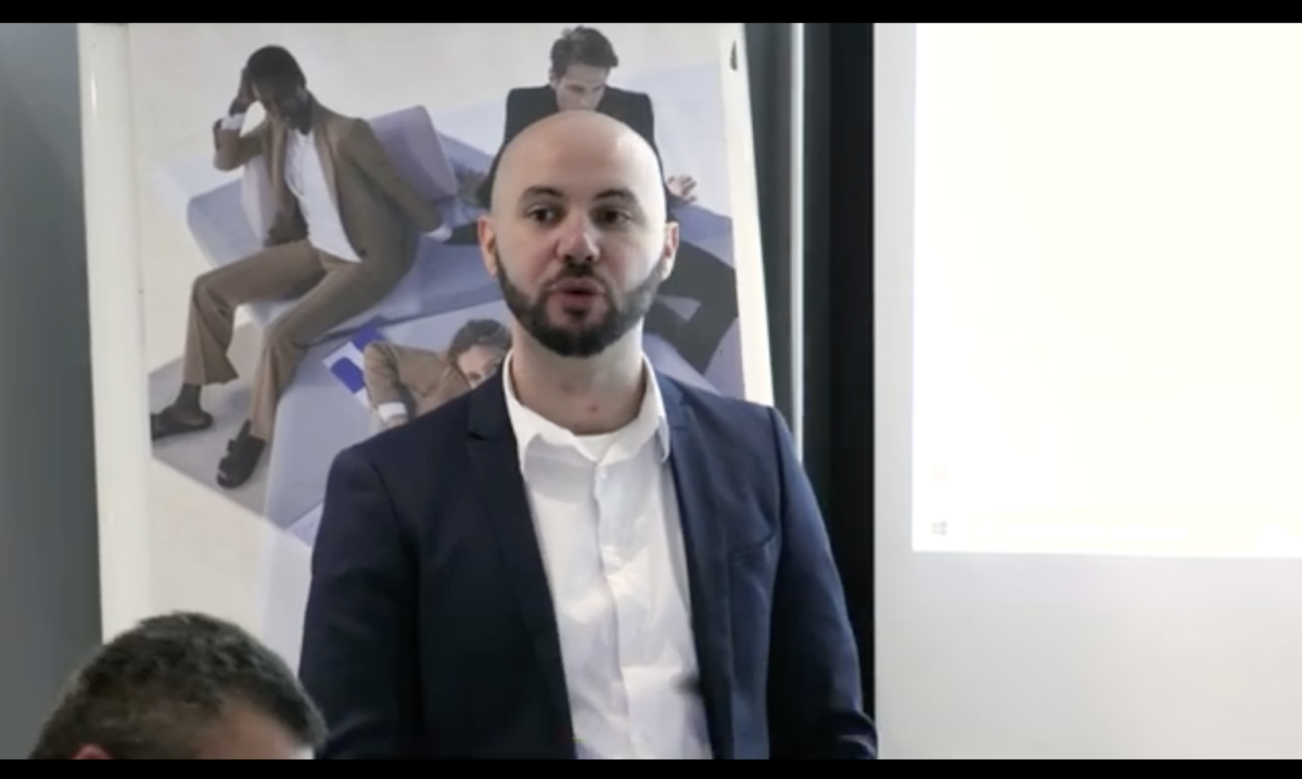 Homme en costume parlant devant un écran.