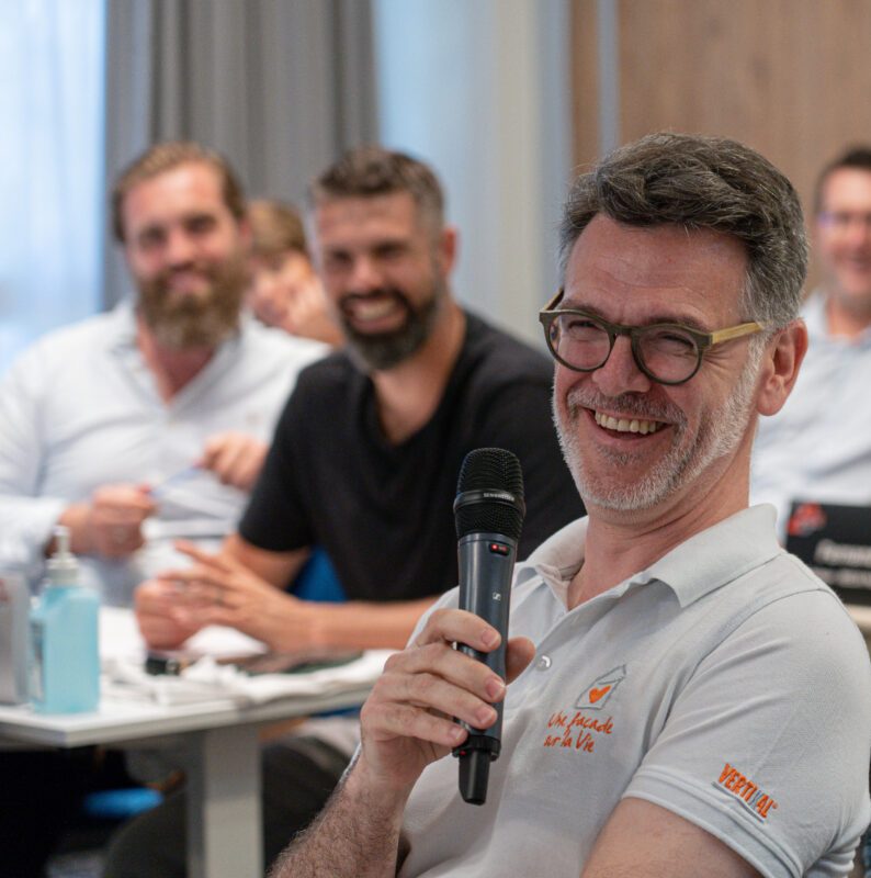 Hommes portant des lunettes et souriant, un homme tenant un microphone.