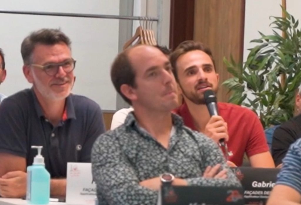 Homme avec lunettes, homme avec microphone, homme en chemise à motifs.